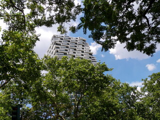 Modernes Apartmenthaus vor blauem Himmel mit weißen Wolken zwischen grünen Baumkronen im Sommer...