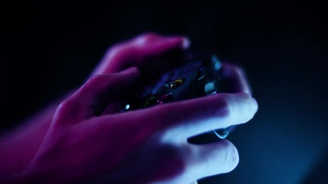 Playing video games in a darkened room with a black background close up on a controller hands quikly blue lens flare