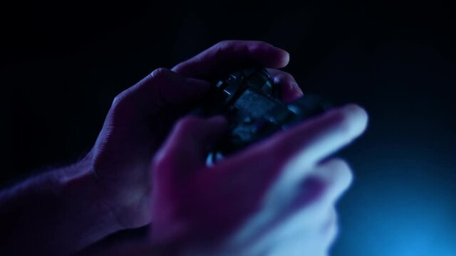 Playing video games in a darkened room small controller buttons facing camera playing quickly with blue lens flare