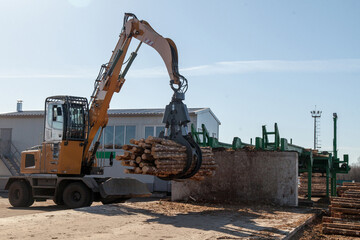 An industrial loader loads logs into a conveyor at a sawmill
