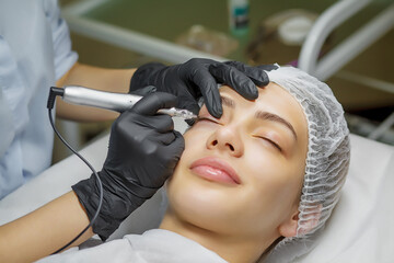 Permanent make up eyeliner procedure, applying on young girl. Close-up. Young beautiful woman making permanent makeup in cosmetology salon. Young girl applying permanent eyeliner in beauty studio