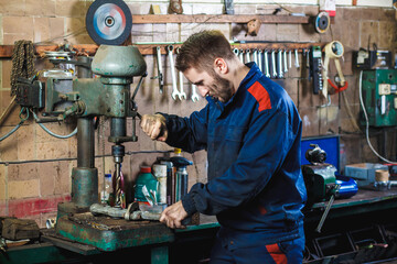 A mechanic drills a detail on a drill press. Workflow mechanic in a car garage. Auto service concept.