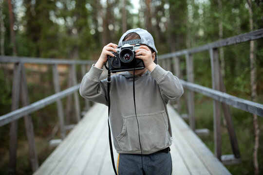 Creative child, child photographer (little boy) with a camera taking pictures of the forest