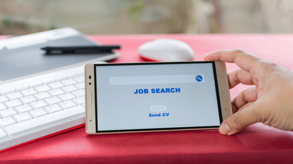 Online job search, woman's hands holding a mobile in which an employment website appears. Work desk with keyboard in the background.