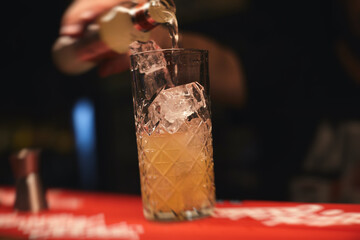 Beautiful row of different colored alcohol cocktails on a party, martini, vodka, and others on decorated catering bouquet table on open air event with bartender in the background