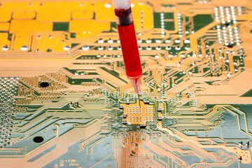 motherboard with contact paths of microcircuit and syringe with needle filled with red liquid,...