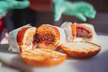 Process of cooking classic burgers with beef on open-air, view of chef hands in  gloves with variety of fillings and ingredients on wooden desk and stove