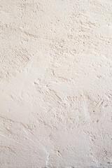 Light beige plastered concrete wall, painted built structure of grungy uneven painted plaster. Abstract light background with with irregularities and bubbles. Vertical view