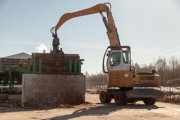 An industrial loader loads logs into a conveyor at a sawmill