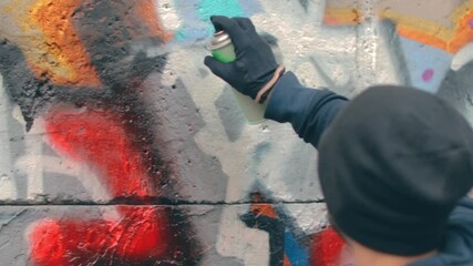 Youthful Guy Vandalizes the Wall Using a Spray Paint Can. Hooligan in Casual Clothing is Drawing Graffiti Outdoors. Youth Movement Crime Related with Street Art. Close-Up View, Dynamic Shot