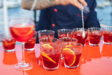 View of alcohol setting on catering banquet table, row line of red colored aperitif alcohol cocktails on a party, negroni and spritz, vodka, and others on decorated catering bouquet table event