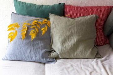 Four cushions on the sofa with branch of yellow leaves as seasonal decoration. Autumn interior
