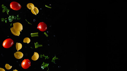 Fototapeta na wymiar Falling italian pasta with cherry tomatoes, parsley and onions, herbs with water drops on a black background, freeze in motion, horizontal photo, banner for design