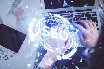 Multi exposure of man's hands typing over computer keyboard and SEO hologram drawing. Top view. Search optimization concept.