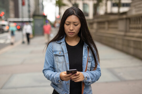 Young Asian woman walking street texting cellphone