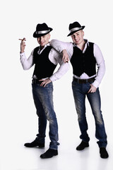 two twin brothers in gangster style posing. hats, vests, white shirts. white background.
