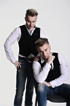 two twin brothers in gangster style posing. hats, vests, white shirts. white background.
