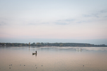 Fototapeta na wymiar Fisherman boat fishing on the Danube river on his rowing boat during a warm autumn afternoon in Zemun, a northern district of Belgrade, capital city of Serbia.