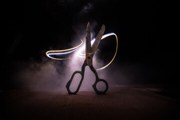 Old tailor`s scissors on wooden table in low light. Artwork decoration with toned foggy backlight. Selective focus
