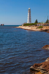 The white lighthouse stands on the seashore. Not far from it is a grounded ship.