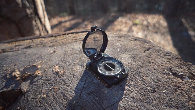 The theme is tourism and technology. Close-up navigation compass black magnetic needle lying on a stump in the forest in sunny weather