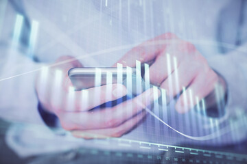 Double exposure of man's hands holding and using a digital device and forex graph drawing. Financial market concept.