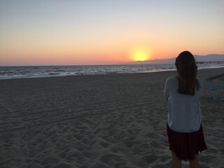 Female tourist overlooking landscape view of empty coastal beach at sunset