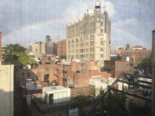 Window view of brownstone buildings under city rainbow