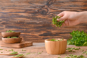 Female hand with dry parsley in bowl on wooden background