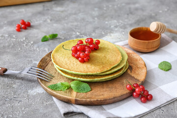 Plate with tasty green pancakes and berries on grey background