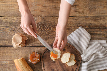 Woman spreading tasty peach jam on bread slice, top view