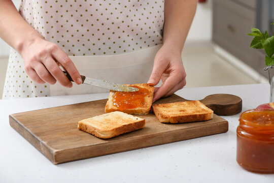 Woman spreading tasty peach jam on bread slice in kitchen