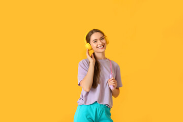 Sporty young woman with headphones and jumping rope on color background