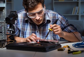 Young repair technician soldering electrical parts on motherboar