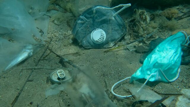Dead Greater weever fish (Trachinus draco) hitting trapped in plastic bag lies inside plastic bag on the seabed among the medical face mask, plastic and other garbage. Plastic pollution of Ocean.  