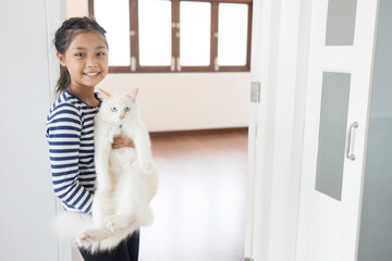 A cute Asian girl is holding her white cat inside a white painted wall house.