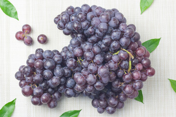 A large bunch of seedless grapes of dark purple lay on a cloth background.