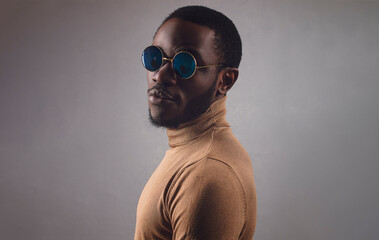 Portrait of handsome bearded young man wearing sunglasses and turtle neck shirt looking over gray background