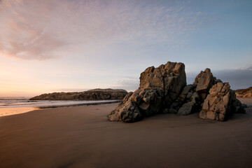 Minimalistic coastal seascape at sunset with rocks on beach. 