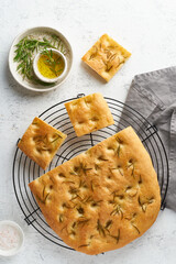 Focaccia, pizza, italian flat bread with rosemary and olive oil on grid on white rustic table,...