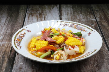 Traditional spicy mixed salad with chopped squid, pork sausage, minced pork, chilly, sweet corn and tomato seasoning with lime juice and fish sauce. Famous spices street food menu in Asia.