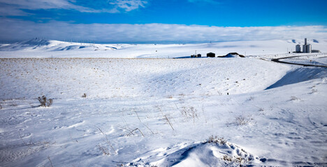 Obraz premium winter field covered in snow with hills and a farm in the distance