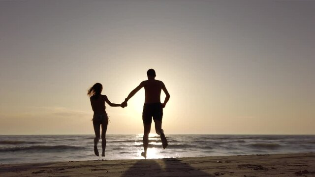 silhouette couple on a beach holding hands and running to the sea. recorded at 60fps