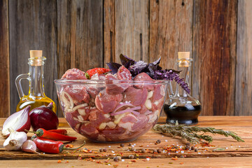 Boneless lamb steak, sliced and marinated with onions, meat in a glass bowl, Basil, chili pepper, marinades on a wooden table, horizontal view, close-up.