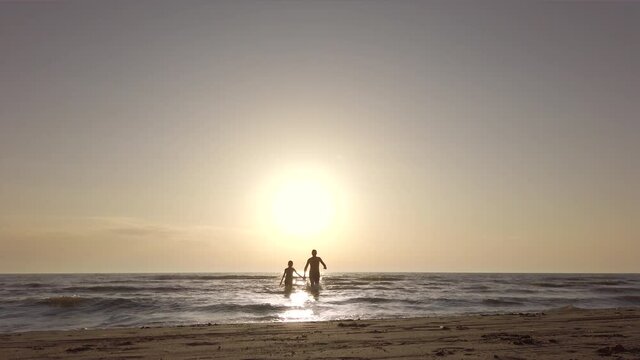 silhouette couple on a beach holding hands and running in the sea towards the camera. recorded at 60fps