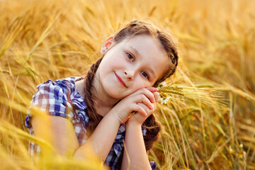 Portrait of a smiling cute little girl in a wheat field in the open air. Nature in the village.