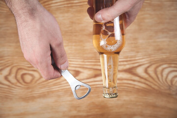 Man holding bottle opener with a beer on the wooden table.
