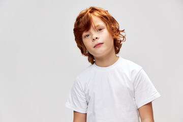 Red haired child in a white t-shirt tilted his head to one side red 