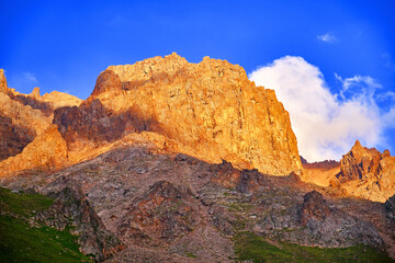 Huge cliffs on the background of blue sky with clouds in the light of setting sun; majestic mountain view at sunset