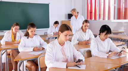 Medical students using mobile phones and writing in notepads during lesson